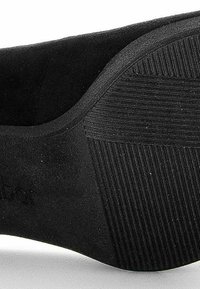 Semelle en caoutchouc noir avec motif de grip texturé, comportant une finition lisse et mate et une légère courbure au talon. Logo embouté sur le côté.