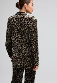 Leopardprint skjorte lavet af blødt, tekstureret stof; har lange ærmer, en krave og en afslappet pasform med en dyb rygkant.