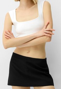 Bílý crop top s čtvercovým výstřihem vyrobený z hladké látky, který je spárován s černou mini sukní s jednoduchým designem a viditelným švem.