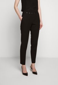 Černé ušité kalhoty s úzkým střihem, jemným leskem a páskem s kovovými detaily. Hladká tkanina, zkrácená délka ke kotníkům.