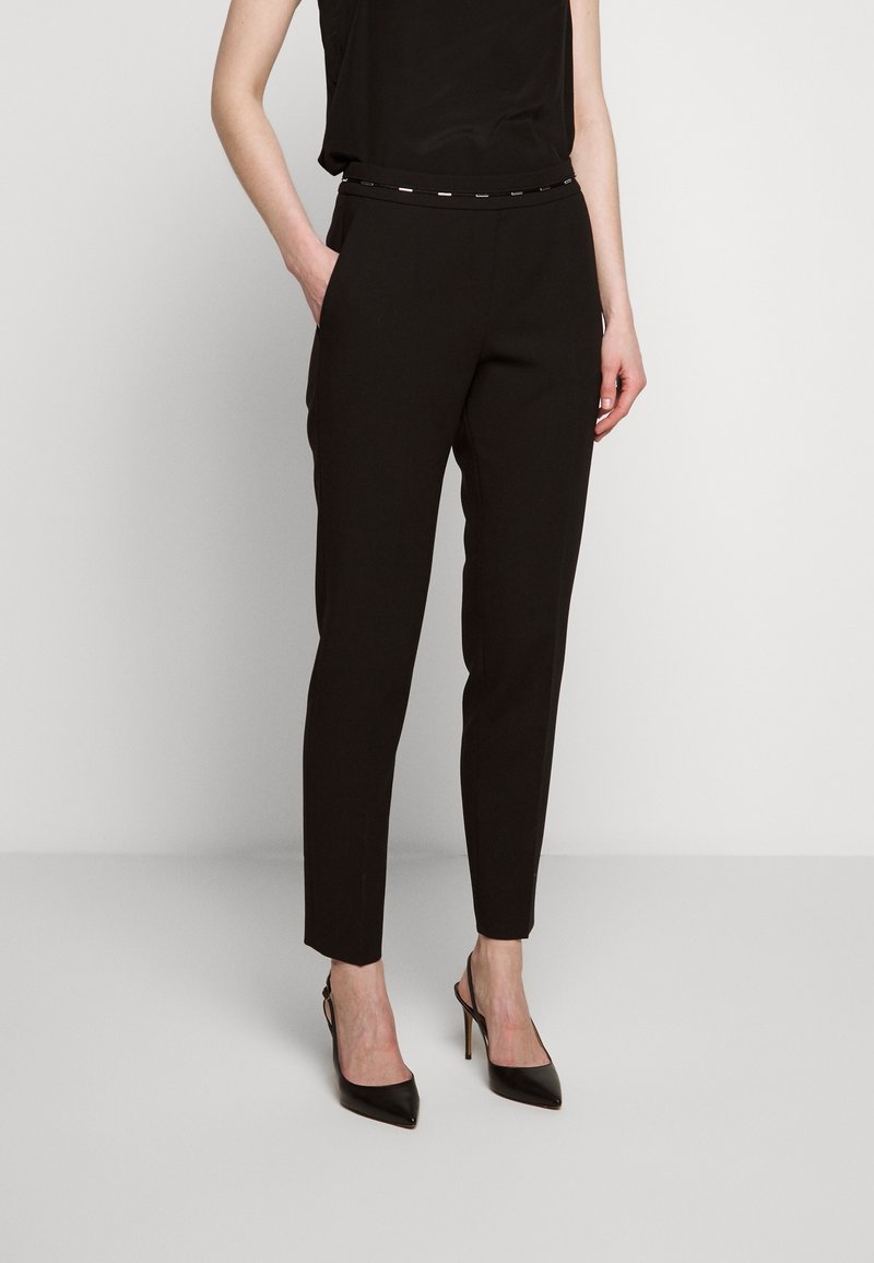 Černé ušité kalhoty s úzkým střihem, jemným leskem a páskem s kovovými detaily. Hladká tkanina, zkrácená délka ke kotníkům.