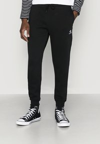 Svarte bomullssweatpants med justerbar snor i livet og smale mansjetter, kombinert med svarte høye sneakers med hvite detaljer.