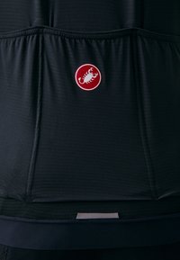 Svart sykkeltrøye laget av teksturert stoff, med en fremtredende rød sirkulær logo med en hvit skorpion i midten.