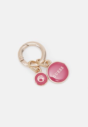 Porte-clés doré avec deux breloques circulaires roses, l'une avec la lettre G et l'autre avec le mot GUESS en blanc.
