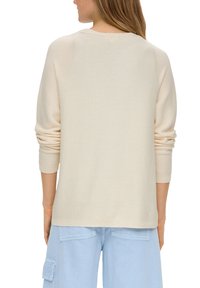 Lichtbeige gebreide trui met een relaxed fit, geribde boorden en een ronde halslijn. De textuur is glad met subtiele horizontale lijnen.