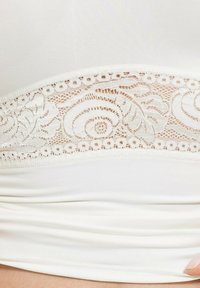 White tank top featuring a textured lace band with floral patterns at the waist. Smooth fabric with a soft, stretchy finish.