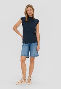 Marineblauwe textuurloze mouwloze top, losse pasvorm, gecombineerd met lichtblauwe denimshorts met een rafelige zoom en witte sandalen met gevlochten banden.