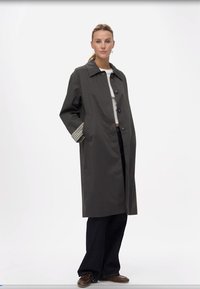 Garšs, tumši pelēks lietussargs ar izgriezumu apkakli, priekšējiem pogām un rūtainām aprocēm. Izgatavots no gludas, ūdensizturīgas vielas.