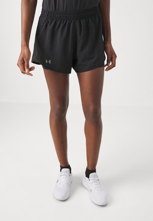 Person wearing black elastic-waist athletic shorts, black ankle socks, and white running shoes standing on a white floor.