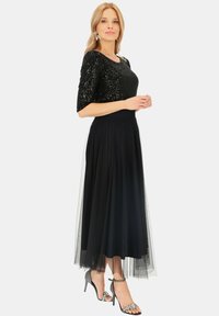 Czarna bluzka z cekinami, krótkie rękawy, połączona z zwiewną czarną spódnicą z tiulu. Srebrne sandały na obcasie dodają elegancji.