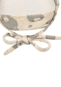 Beige and gray patterned fabric tied in a bow on a textured fabric edge, with visible stitching on a white background.