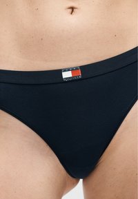 Κοντινή λήψη της κάτω κοιλιάς ενός ατόμου που φοράει μαύρα εσώρουχα με μικρό λογότυπο Tommy Hilfiger στο κέντρο της μέσης.