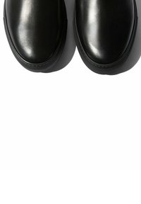 Zapatos de cuero negros con puntera redonda, acabado suave y suelas de goma texturizadas. Diseño minimalista sin adornos visibles.