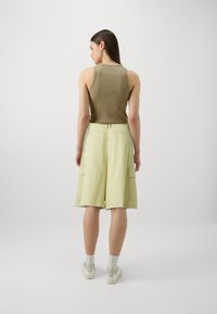 Oliven grønn ribbestrikket tanktop sammen med lysegule knelange shorts med sidelommer. Hvite joggesko og ankelstrømper fullfører antrekket.