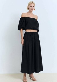 Tenue noire en deux pièces comprenant un haut court à épaules dénudées avec des manches bouffantes et une longue jupe évasée assortie avec une taille à cordon.