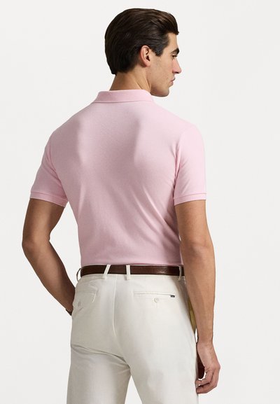 Tricou polo roz cu mânecă scurtă, fabricat din bumbac ribatat, cu guler clasic și croi slim, asortat cu pantaloni albi și o curea maro.