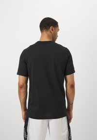 Camiseta negra de manga corta con cuello redondo, hecha de una tela suave, vista desde la parte de atrás. Sin patrones ni logotipos visibles.
