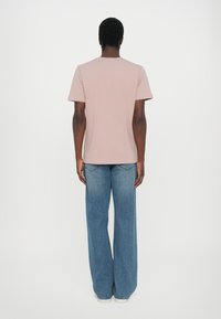 Helles rosa Baumwoll-T-Shirt mit Rundhalsausschnitt und kurzen Ärmeln, kombiniert mit blauen weit geschnittenen Jeans. Einfaches Design, ohne Muster oder Akzente.