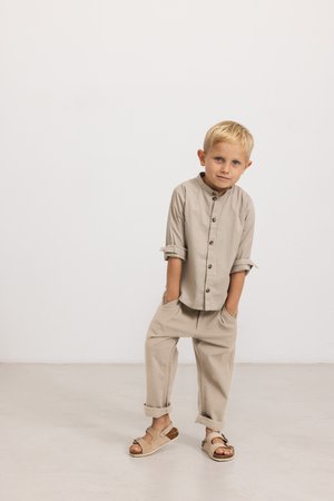 Camisa de algodón beige con mangas enrolladas y botones de madera, combinada con pantalones holgados beige y sandalias color tostado con un acento marrón.