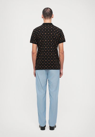 Μαύρο πόλο μπλουζάκι με πολύχρωμα γεωμετρικά σχέδια, σε συνδυασμό με ανοικτό μπλε παντελόνι με ρίγες, απεικονιζόμενο από πίσω.