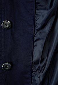 Laivastonsininen kangas, jossa on sileä pinta, pyöreä musta nappi ja kerrostettu sivuosa. Materiaali vaikuttaa kevyeltä ja kestävältä.