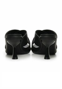 Mules negras de punta abierta con un acabado texturizado, que presentan un tacón curvado y un diseño recortado en los laterales. Forro interior suave visible.