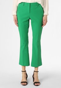 Groene flared broek met een gladde textuur, voorzien van een knoopsluiting en riemlussen. Gecombineerd met zwarte sandalen met bandjes.