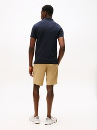 Marineblå polo skjorte, kaki shorts og hvite joggesko. Enkelt design, korte ermer og klassisk passform. Glatt tekstur og ingen synlige mønstre.