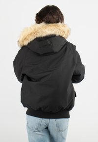 Parka noire avec capuche en fourrure, poignets côtelés et ourlet élastique. Le tissu est lisse avec une finition mate.