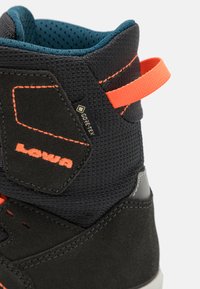 Zwarte en donkergrijze wandelschoen met textuur nylon en suede, met felle oranje accenten en een trekhaak; GORE-TEX-label zichtbaar.