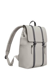 Zaino grigio chiaro, realizzato in materiale liscio. Presenta un flap pieghevole, due tasche anteriori con zip e bretelle e dettagli grigio scuro.