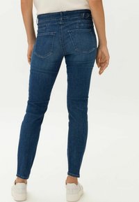 Jeans ajustados de mezclilla en azul oscuro con una textura suave, diseño de cinco bolsillos y sutiles detalles de costura en la parte posterior.
