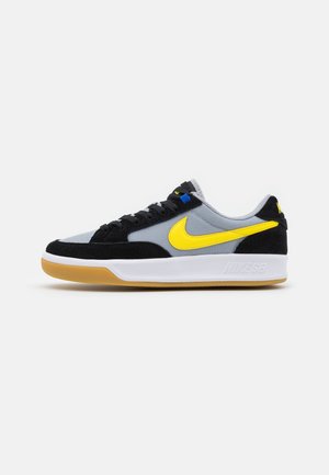 Basket basse Nike avec tige noire et grise, logo Swoosh jaune, semelle intermédiaire blanche et semelle extérieure en caoutchouc naturel.