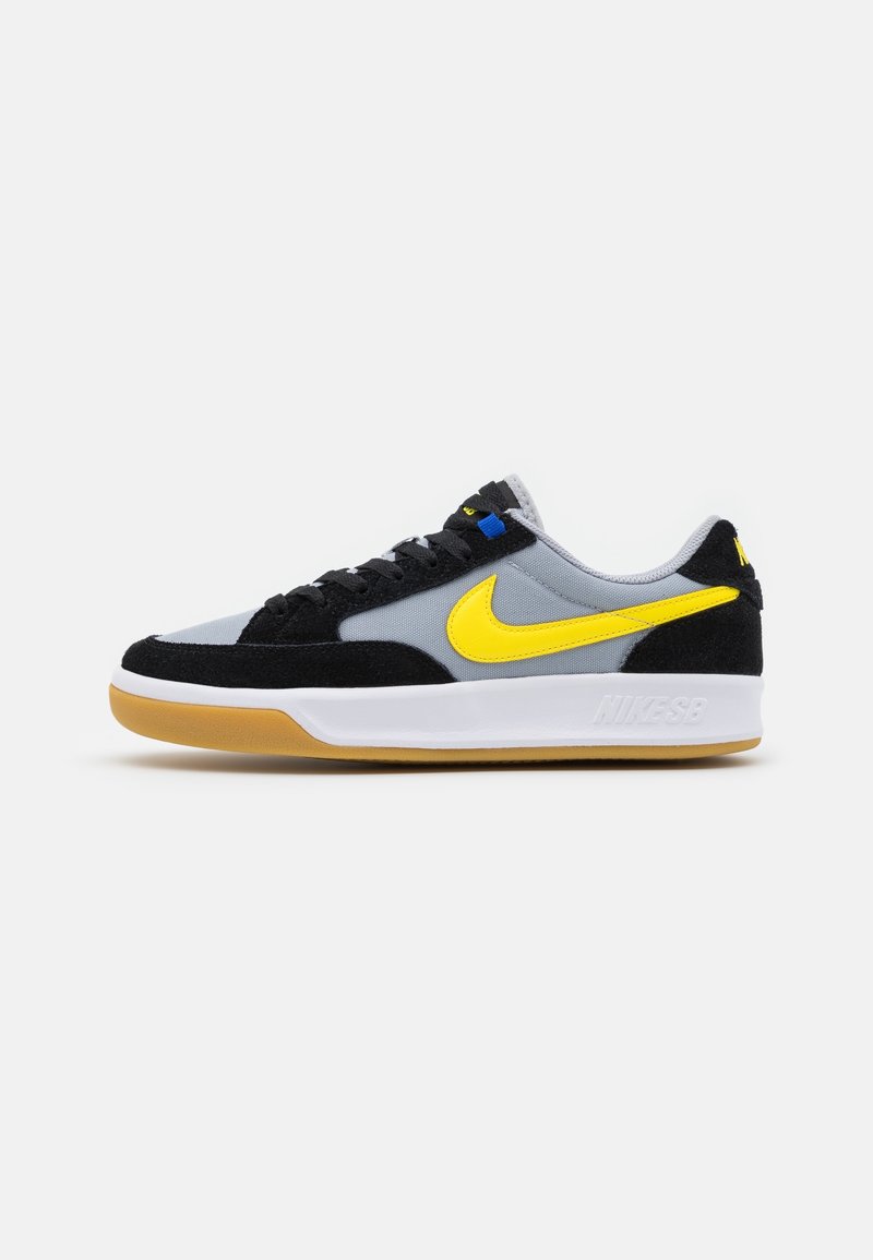 Basket basse Nike avec tige noire et grise, logo Swoosh jaune, semelle intermédiaire blanche et semelle extérieure en caoutchouc naturel.