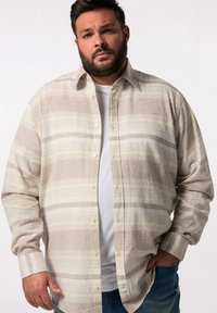 Camisa de botón a rayas marrón claro y crema con cuello y mangas largas, hecha de una tela texturizada, llevada sobre una camiseta blanca.