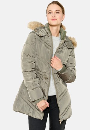Chaqueta acolchada en verde olivo con cremallera frontal, capucha desmontable con borde de piel y detalles de costuras diagonales. Diseño ligero y aislante.
