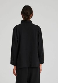 Cămașă neagră, mâneci lungi, manșete cu nasturi, croială lejeră, detaliu la guler, realizată dintr-un material moale cu cusături minime, design simplu fără modele.