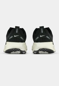 Zapatillas deportivas negras con un upper texturizado y acentos reflectantes, que presentan una suela blanca y gris, un talón texturizado y un patrón de suela de goma.