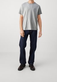 Harmaan puuvillapaita, jossa on pyöreä kaula-aukko ja logopatch, yhdistetty tummansinisiin farkkuihin, joissa on kontrastiväriset saumat, sekä mustiin saappaisiin.