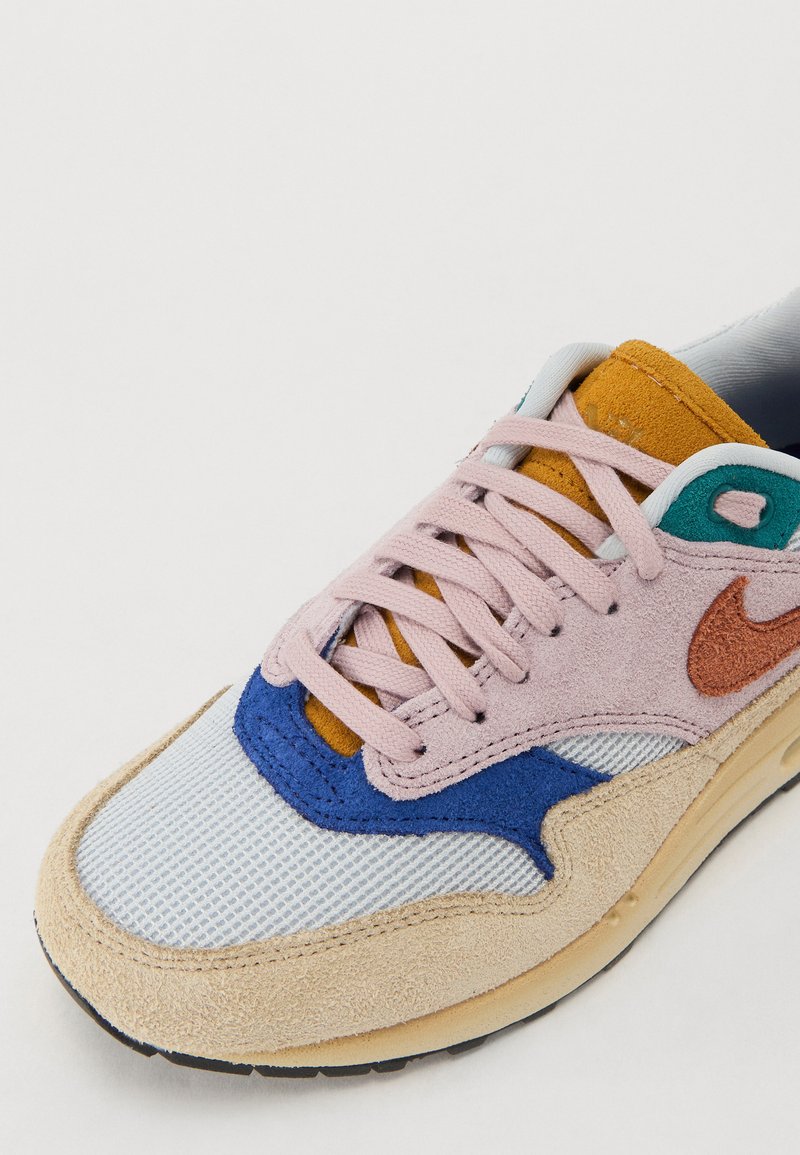 Sneaker met een mix van materialen: roze suede, blauwe mesh en beige suede. Accentkleuren zijn oranje en teal, met zichtbare veters en stiksels.