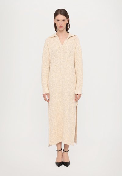 Robe en tricot beige à manches longues et col, avec une fente latérale et des poignets côtelés. Texture lisse avec un motif subtil.
