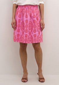 Rosa kjol med ett strukturerat blommönster, utrustad med elastisk midja och knälång design. Bärs med bruna sandaletter med remmar.