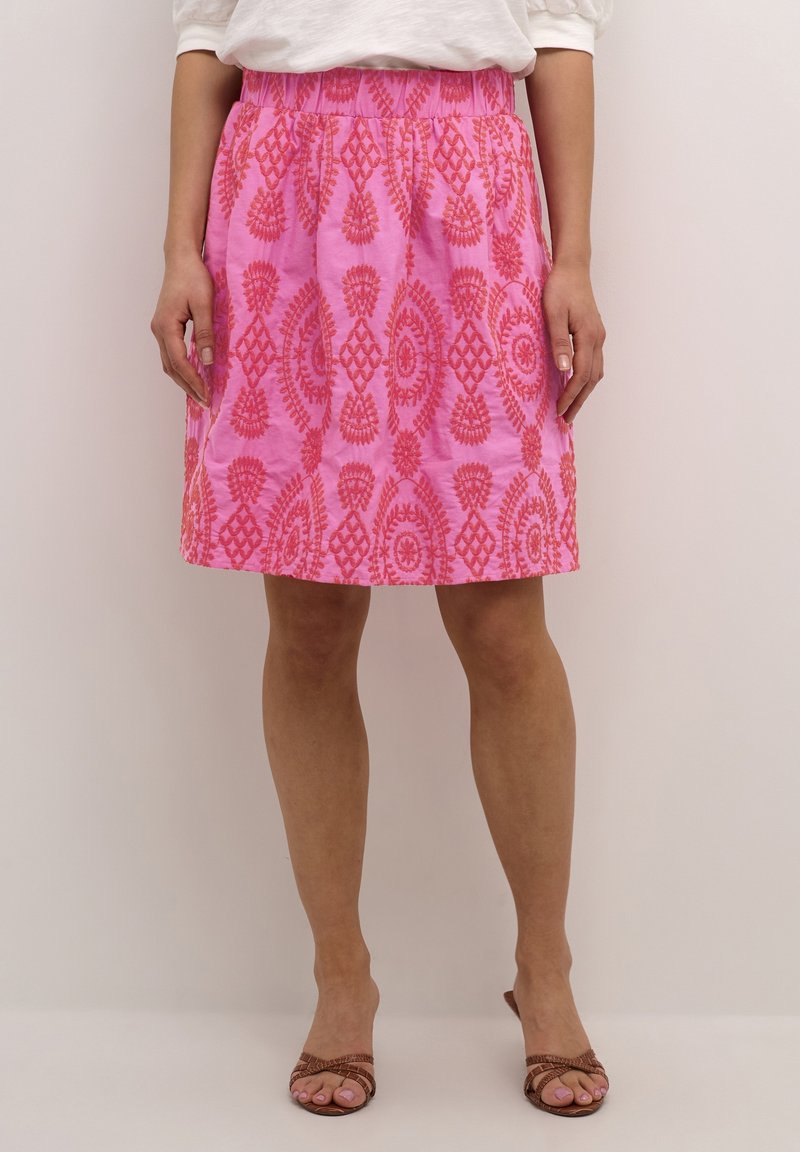 Rosa kjol med ett strukturerat blommönster, utrustad med elastisk midja och knälång design. Bärs med bruna sandaletter med remmar.