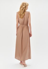 Sukienka maxi w jasnobeżowej tkaninie o luźnym kroju, z talią cinched i zawiązaniami na ramionach. Posiada boczne rozcięcie dla większej swobody ruchu.