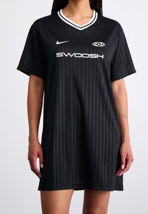 Femme portant une robe de sport noire à fines rayures avec un col blanc bordé et les logos blancs "SWOOSH" et Nike sur la poitrine.