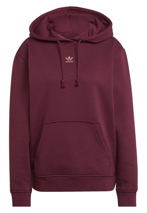 Osoba ubrana w bordową bluzę z kapturem Adidas z kieszenią z przodu i sznurkami, zestawioną z kremowymi spodniami, skróconymi przy szyi i udach.