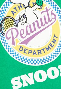 Camiseta verde con un gráfico redondo que presenta el logo de "Peanuts", un motivo de tenis y el texto "SNOOPY" en una fuente blanca en negrita.