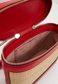 Czerwona skórzana torebka na suwak z plecionym słomianym korpusem; wnętrze wyłożone gładką tkaniną z wieloma przegródkami na karty. Złote ozdobne elementy.