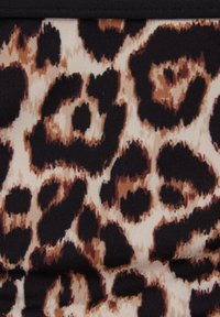 Tkanina w nadruk w panterkę o jasnym tle z ciemnobrązowymi i czarnymi plamkami, o fakturze żebrowanej powierzchni. Obrzeżona czarną lamówką.