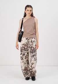 Top asimetric pe un umăr, combinat cu pantaloni oversized de culoare bej deschis, cu un model în buline maronii. O geantă neagră și pantofi negri completează ținuta.